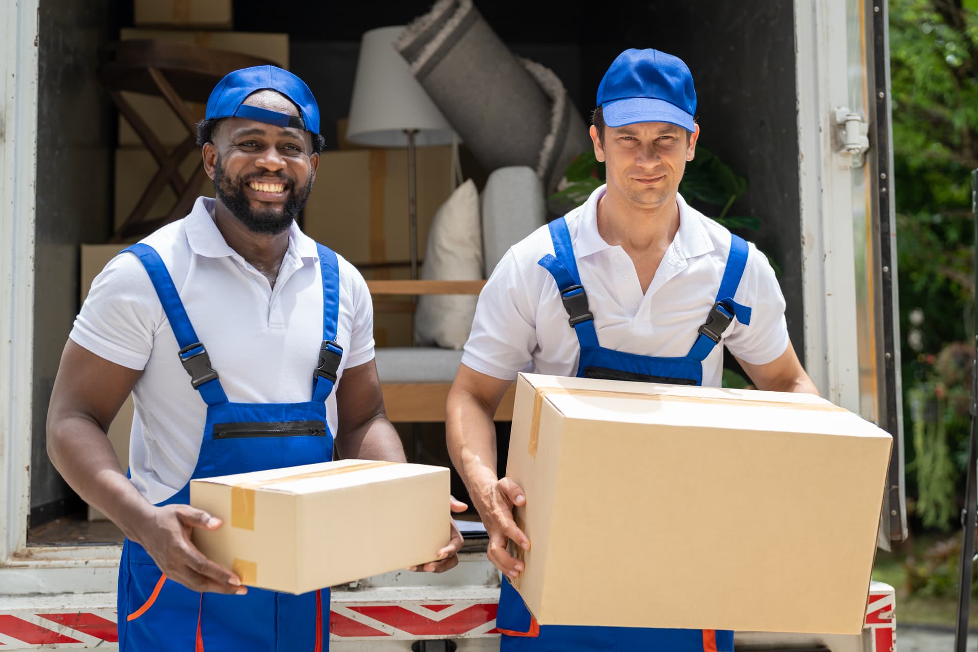 Two licensed professional movers in uniform carrying boxes through a St. Petersburg home